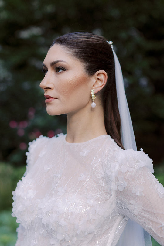 Bride wearing gold and baroque pearl wedding earrings and delicate veil.