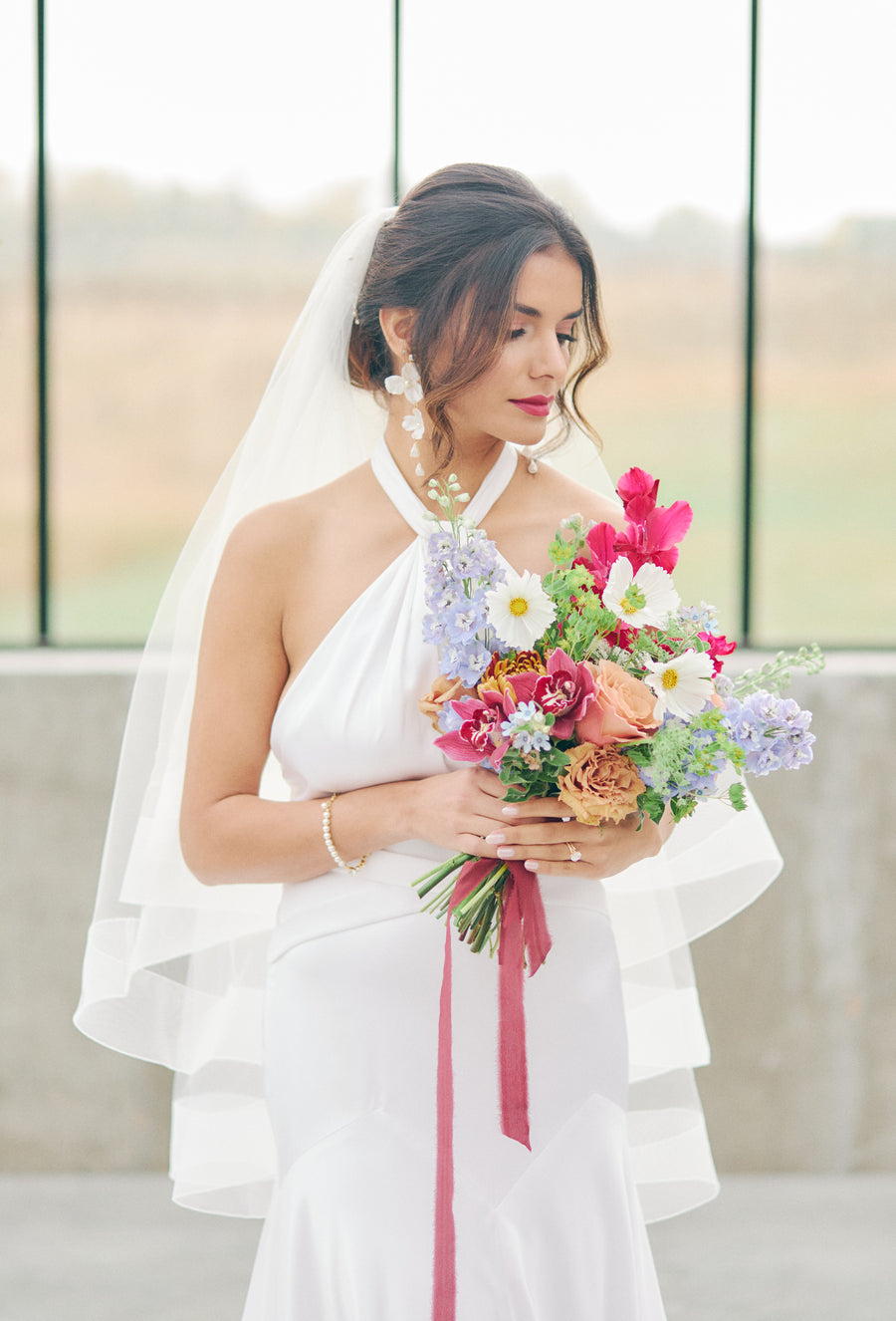 Bridal wearing statement wedding earrings and holding a bouquet.