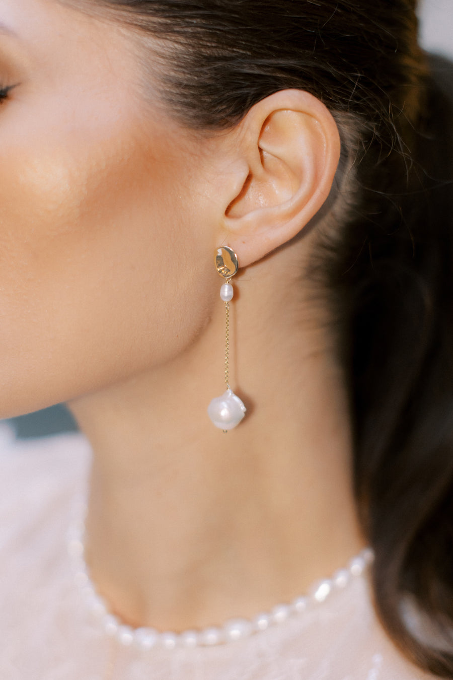 Close up of bride wearing long baroque pearl wedding earrings. 