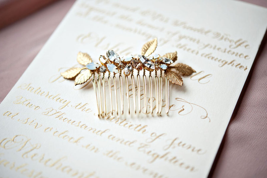 A luxury crystal and golden leaf bridal comb placed over an elegant invitation.